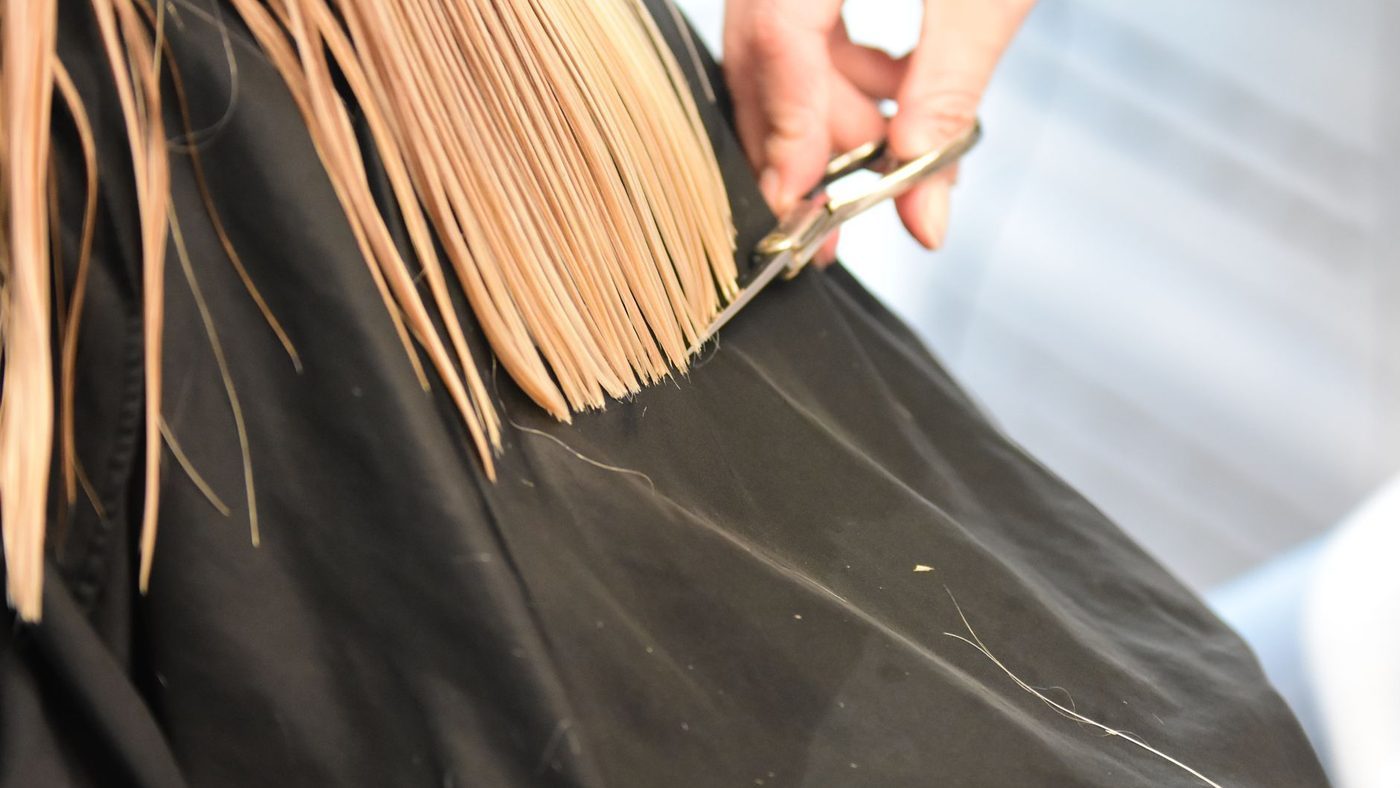 Coiffeur coupant des cheveux blonds aux ciseaux, en gros plan